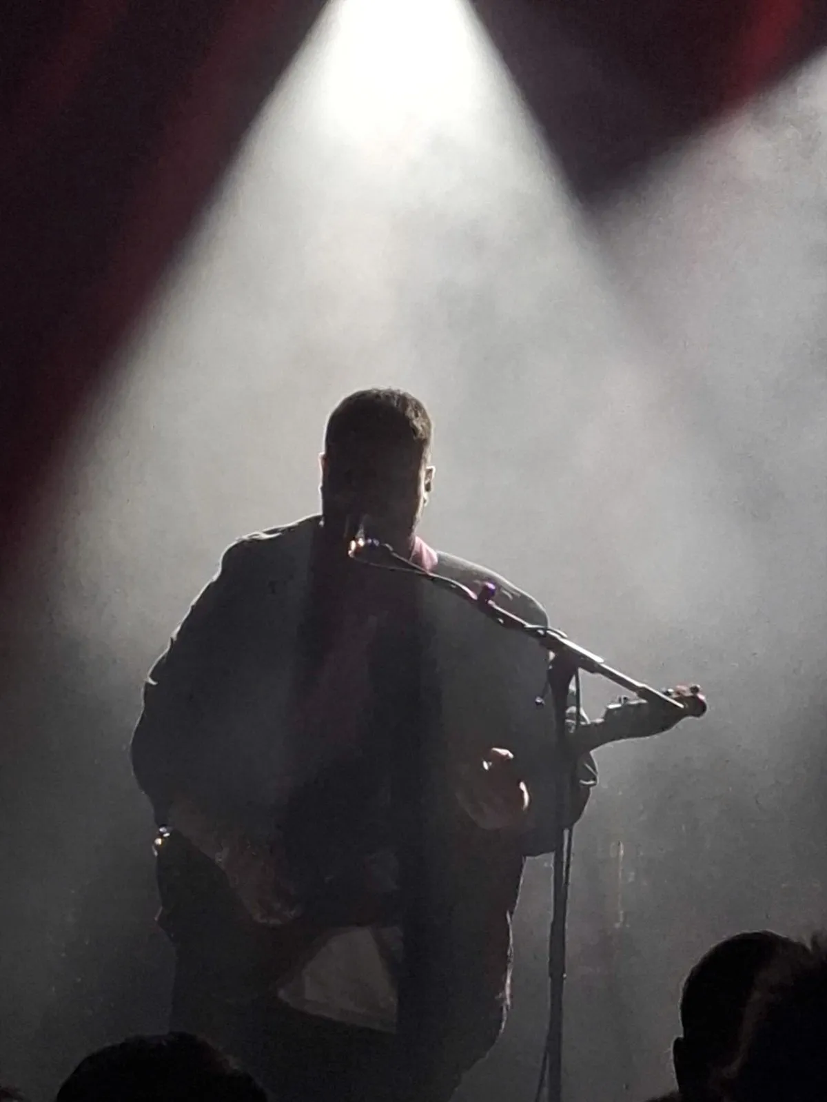 The singer in silhouette under a single spotlight, haze everywhere