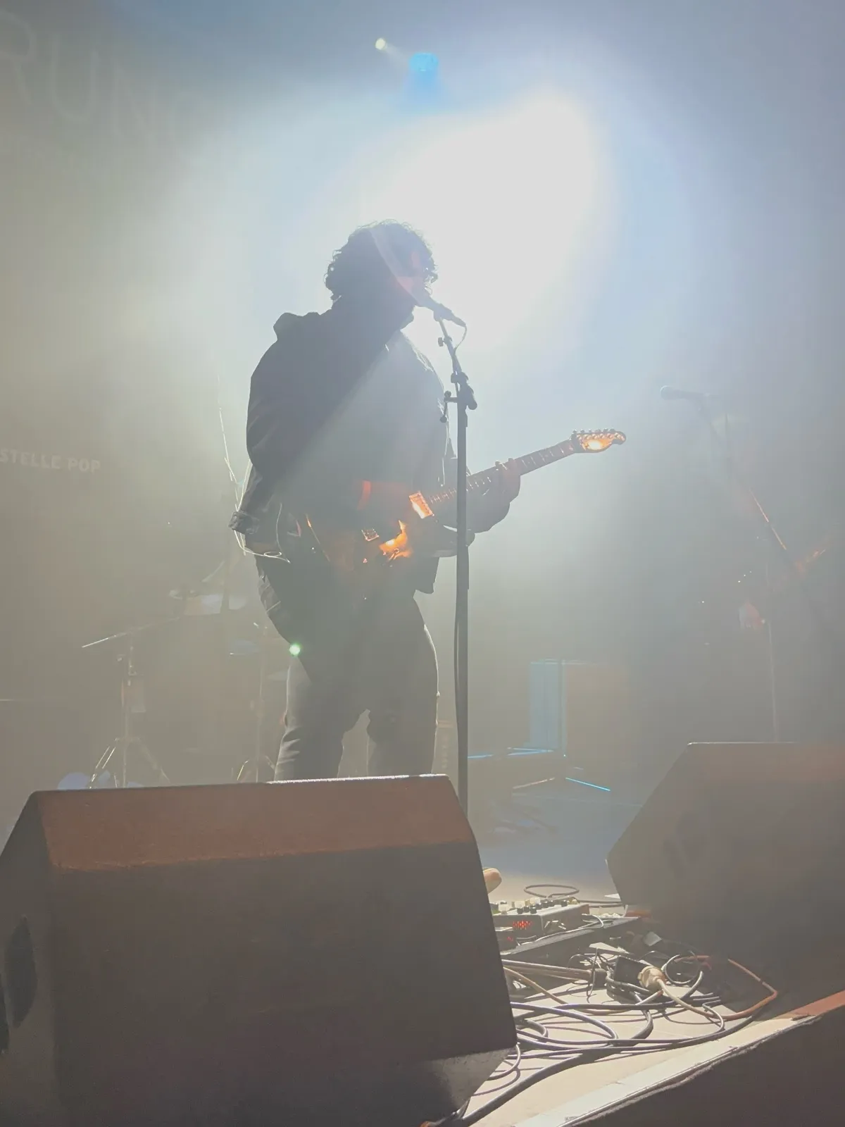 Singer and guitarist in silhouette at the microphone, haze and a bright spotlight behind